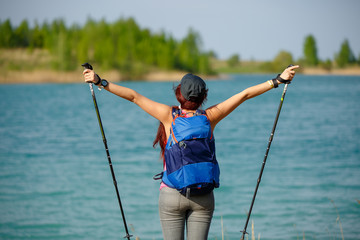Image of back of sporty woman with walking sticks and backpack on lake background