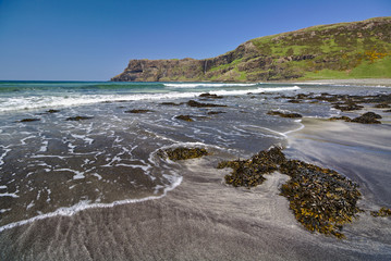 Talisker Bay, Isle of Skye, Scotland - Sandy beach with seaweed in the foreground and white surf and sea cliffs in the distance