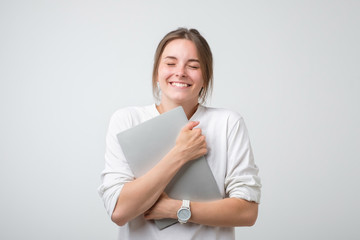Cheerful caucasian woman in white t-shirt holding laptop computer and smiling.