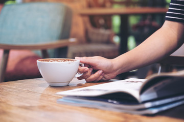 Closeup image of a woman reading a magazine with coffee cup on table in cafe