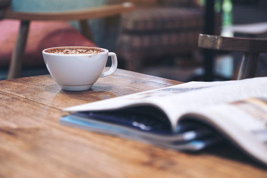 Closeup image of a magazine with coffee cup on wooden table in cafe