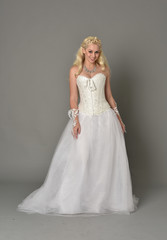 Fototapeta premium full length portrait of blonde girl wearing white corset gown. standing pose on grey studio background.