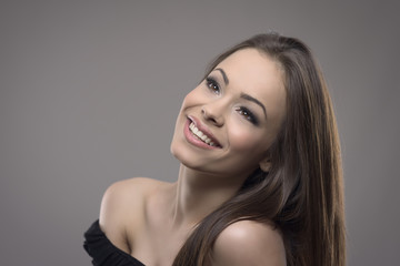 Studio portrait of fresh gorgeous woman with perfect skin daydreaming and looking up at copyspace over gray background. 