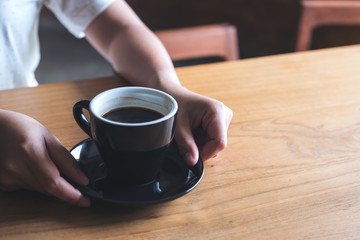 Closeup image of woman's hands holding and giving a cup of hot coffee on wooden vintage table