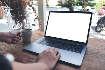 Mockup image of a woman using laptop with blank white desktop screen while drinking hot coffee in cafe