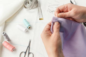 Closeup of skilled tailor hands marking and measuring fabric while making clothes.