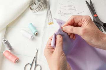 Closeup of skilled tailor hands marking and measuring fabric while making clothes.