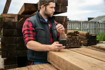 Lumber yard worker, carpenter at wood yard counts inventory with mobile device
