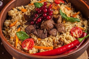 Uzbek restaurant concept, Uzbek food feast. Uzbek pilaf made from beef, lamb, chicken, in large earthenware, plate, next to vegetables. Copy space