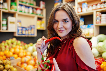 Girl in red holding hot chili peppers on fruits store.