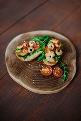 Fototapeta na wymiar Tasty snack of open sandwich with avocado, shrimps and arugula on wooden cutting board. Top view.Breakfast concept