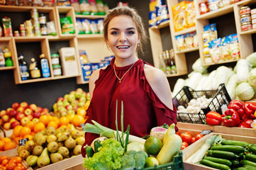 Girl in red holding different vegetables on fruits store.