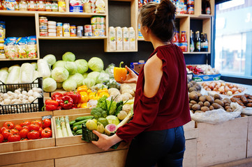 Girl in red holding different vegetables on fruits store.
