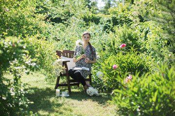 Naklejka na ściany i meble young woman is resting in the garden on a chair with a cup of tea