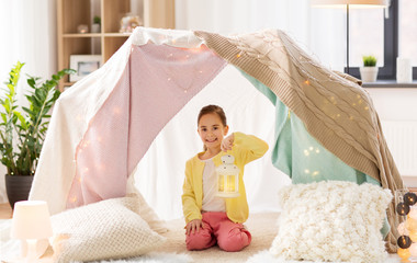 childhood and hygge concept - happy little girl with christmas lantern in kids tent at home