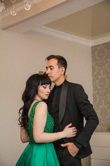 Fototapeta premium elegant guy and girl in luxury suites. Brown-haired woman in an emerald expensive dress and a guy in a black tuxedo. The life of rich people.