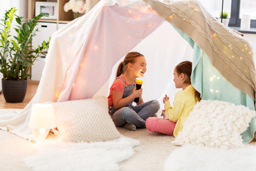 childhood, hygge and friendship concept - little girls with torch light having fun in kids tent or teepee at home © Syda Productions