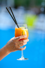 Woman holds orange cocktail on swimming pool background