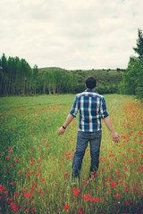 Hombre joven disfrutando de un día de primavera en un campo de trigo y amapolas 