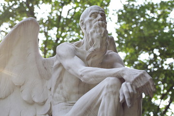 Cemetery sculpture Chronos Archangel Gabriel Uriel sitting in front of blurred foliage