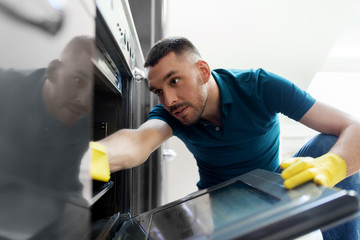 household and people concept - man wiping table with cloth cleaning inside oven at home kitchen