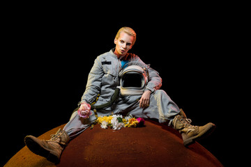 attractive spacewoman in spacesuit with flowers and helmet sitting on planet