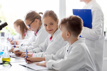 Fototapeta premium education, science and children concept - teacher and kids studying chemistry at school laboratory and writing to workbooks