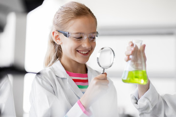education, science and children concept - girl with magnifier studying test tube with chemical at...