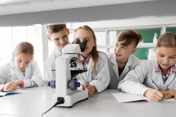 education, science and children concept - kids or students with microscope studying biology at school laboratory