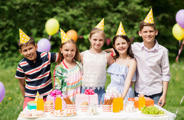 holidays, childhood and celebration concept - happy kids hugging on birthday party at summer garden