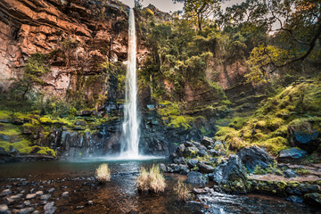 Full view of the red cliffs, plunge pool, and moss and fern covered rocks at Lone Creek Falls in Mpumalanga, South Africa