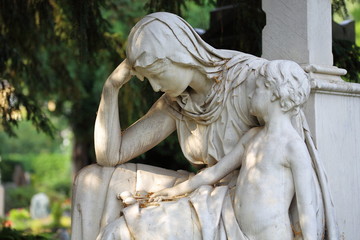 Cemetery sculpture Mourning mother sitting with child standing by the side against blurred background