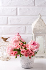 Pink roses flowers and decorative  lanterns  against  white brick wall.