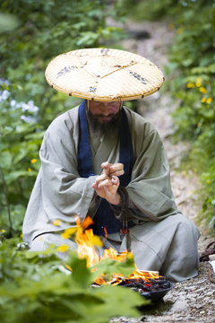 European man with beard and japanese robe makes fire ceremony in front of Great Waterfall in Austria
