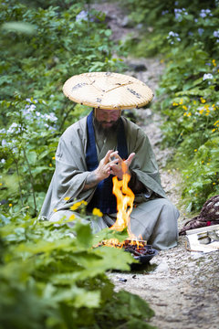 European man with beard and japanese robe makes fire ceremony in front of Great Waterfall in Austria