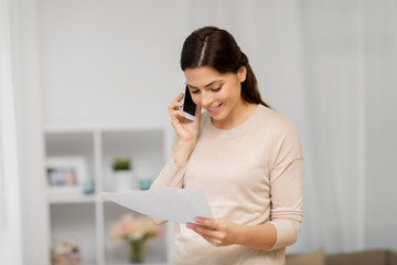 people, freelance and education concept - happy smiling woman with papers on smartphone calling at home