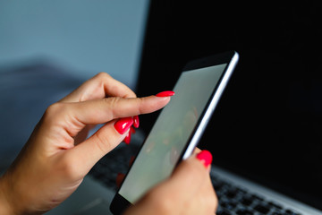 Lovely blonde woman phoning with her smartphone lying on her bed next to her notebook. Mobile phone with blank screen in female hands. Сoncept of chating, mobile banking, online payment.