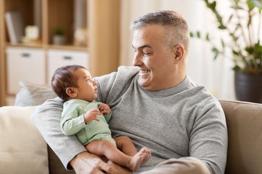 family, fatherhood and people concept - happy father with little baby boy sitting on sofa at home