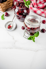 Homemade preserved cherry and mint jam, with fresh cherries on white marble background copy space