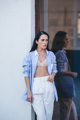 Naklejka premium A beautiful woman in a shirt and pants is standing by the mirror window of the balcony of the building. 