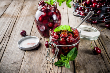 Homemade preserved cherry and mint jam, with fresh cherries on rustic old wooden background copy space