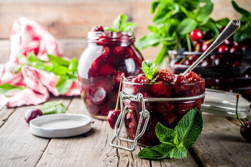 Homemade preserved cherry and mint jam, with fresh cherries on rustic old wooden background copy space