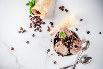Homemade coffee ice cream, served with coffee beans and mint leaves, with ice cream cones and spoons in the picture. White marble background,