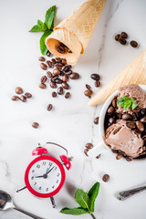 Homemade coffee ice cream, served with coffee beans and mint leaves, with ice cream cones and spoons in the picture. White marble background,