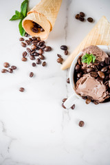 Homemade coffee ice cream, served with coffee beans and mint leaves, with ice cream cones and spoons in the picture. White marble background,