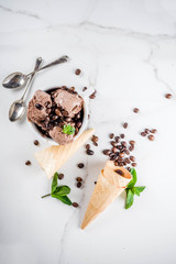 Homemade coffee ice cream, served with coffee beans and mint leaves, with ice cream cones and spoons in the picture. White marble background,