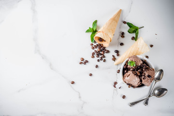Homemade coffee ice cream, served with coffee beans and mint leaves, with ice cream cones and spoons in the picture. White marble background,
