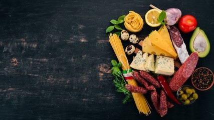 Assortment of sausage, cheese and fresh vegetables. Italian cuisine. On a black wooden background....