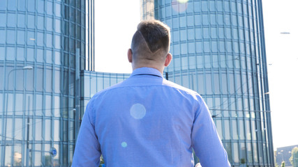 Young handsome businessman in blue shirt walking along the street, skyscraper background.
