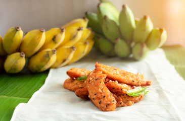 Close up view of fried banana sprinkled with black sesame seeds. Pile on white cloth. With light from the side.